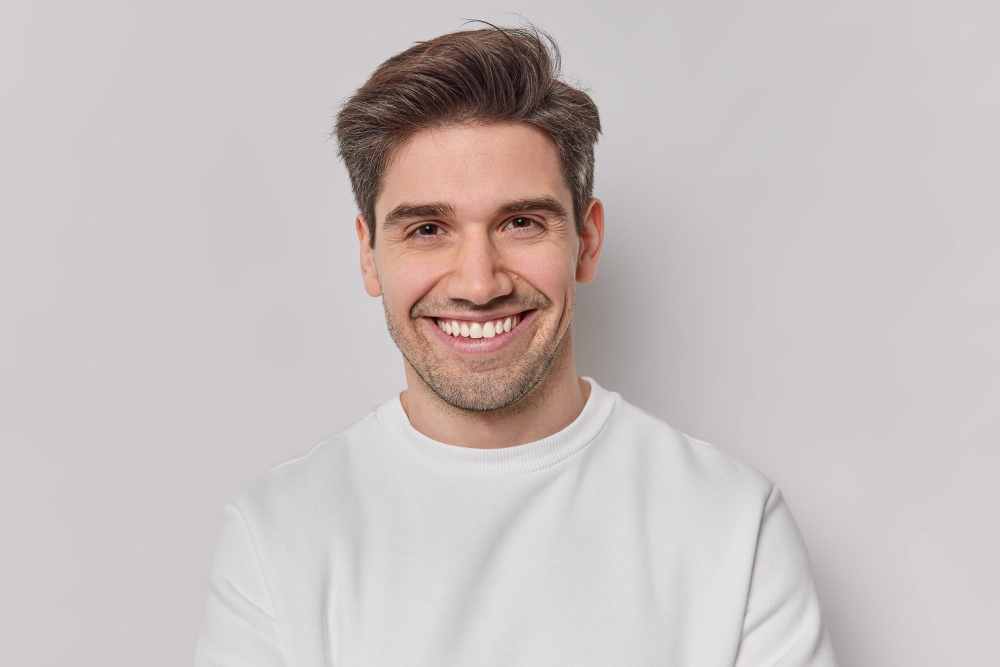 portrait-handsome-man-with-dark-hairstyle-bristle-toothy-smile-dressed-white-sweatshirt-feels-very-glad-poses-indoor-pleased-european-guy-being-good-mood-smiles-positively-emotions-concept